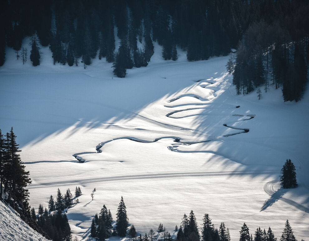 Über eine verschneite Hochfläche auf der Wurzeralm in Spital am Pyhrn in der Uraubsregion Pyhrn-Priel ziehen sich die tief in den Schnee eingeschnittenen Bögen eines mäandernden Baches.