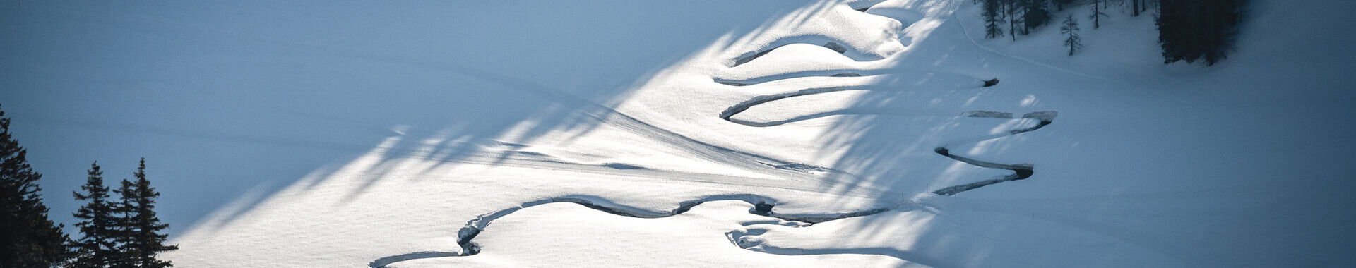 Über eine verschneite Hochfläche auf der Wurzeralm in Spital am Pyhrn in der Uraubsregion Pyhrn-Priel ziehen sich die tief in den Schnee eingeschnittenen Bögen eines mäandernden Baches.